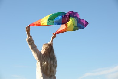 Photo of Woman holding bright LGBT flag against blue sky