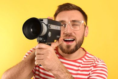 Young man with vintage video camera on yellow background, focus on lens