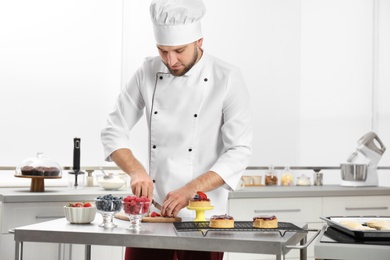 Photo of Male pastry chef cutting berries at table in kitchen