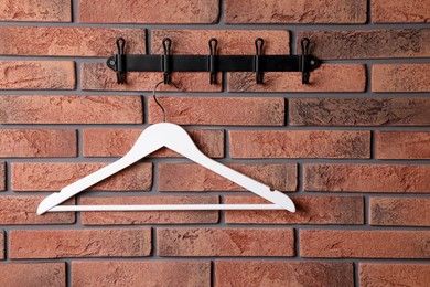 Photo of Hook rack with white clothes hanger on red brick wall