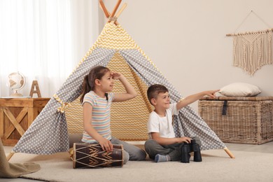 Cute little children playing in toy wigwam at home