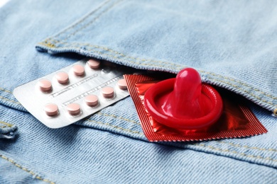Red condom and birth control pills in pocket of jeans, closeup. Safe sex concept