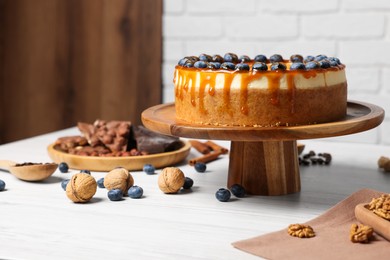 Delicious cheesecake with caramel and blueberries on white wooden table indoors