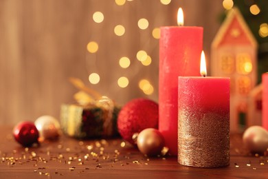 Beautiful burning candles with Christmas decor on wooden table against blurred festive lights, space for text