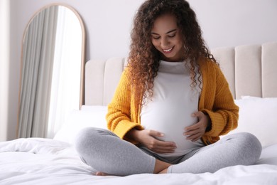 Pregnant young African-American woman sitting on bed at home