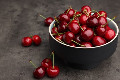 Photo of Bowl with ripe sweet cherries on dark grey table, space for text