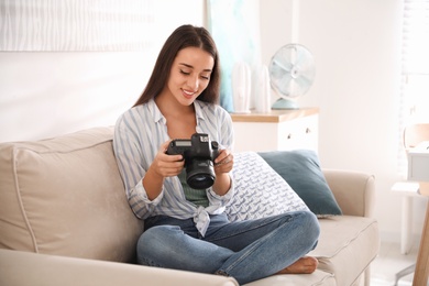 Young photographer with professional camera on sofa indoors