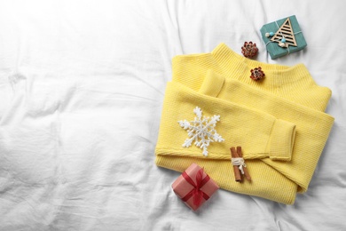 Photo of Yellow warm sweater and decorations on white bedsheet, flat lay. Space for text