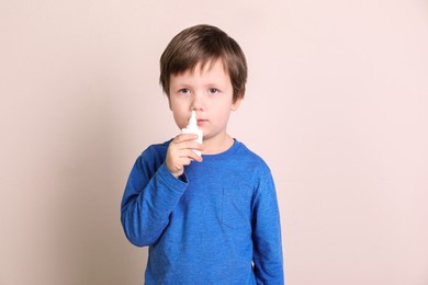 Sick little boy using nasal spray on light background