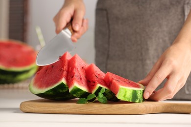 Woman cutting delicious watermelon at white wooden table indoors, closeup