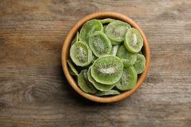 Bowl with slices of kiwi on wooden background, top view. Dried fruit as healthy food