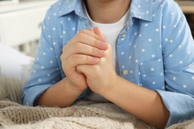 Girl with clasped hands praying near bed, closeup