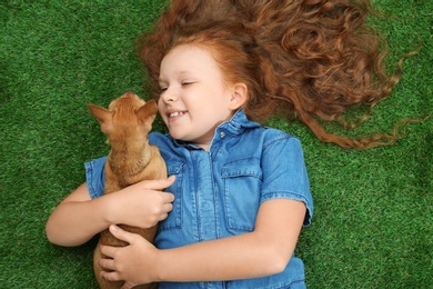 Little girl with her Chihuahua dog lying on grass, top view. Childhood pet