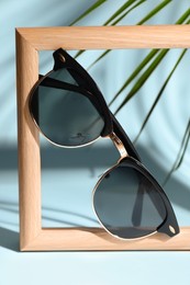 Stylish sunglasses near photo frame on light blue background
