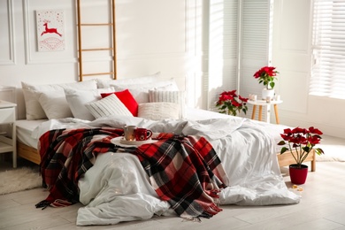 Photo of Christmas bedroom interior with red woolen blanket and poinsettias