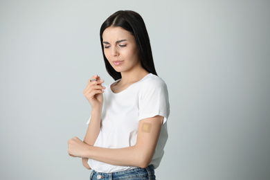 Emotional young woman with nicotine patch and cigarette on light grey background