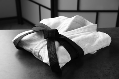 Martial arts uniform with black belt on grey stone table indoors