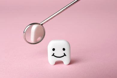 Decorative tooth with funny face and dentist mirror on pink background, closeup