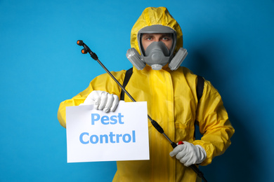 Man wearing protective suit with insecticide sprayer holding sign PEST CONTROL on blue background