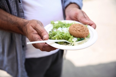 Poor man with donated food on plate outdoors, closeup