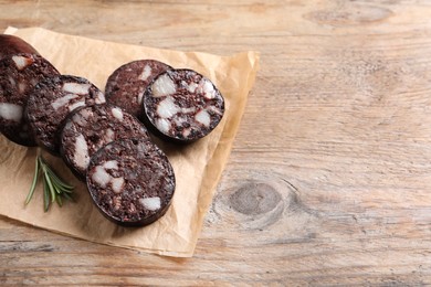 Slices of tasty blood sausage with rosemary on wooden table, space for text