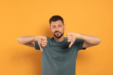 Man showing thumbs down on orange background
