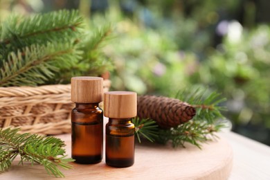 Bottles of pine essential oil, cone and branches on wooden table, closeup. Space for text