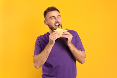 Photo of Young man eating tasty sandwich on yellow background