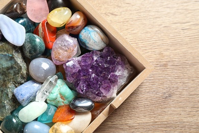 Photo of Box with different beautiful gemstones on wooden table, flat lay