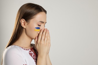 Photo of Sad young Ukrainian woman with clasped hands on beige background, space for text