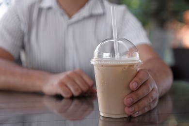 Man with plastic takeaway cup of delicious iced coffee at table in outdoor cafe, closeup. Space for text