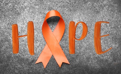 Orange ribbon and word HOPE on grey background, top view 