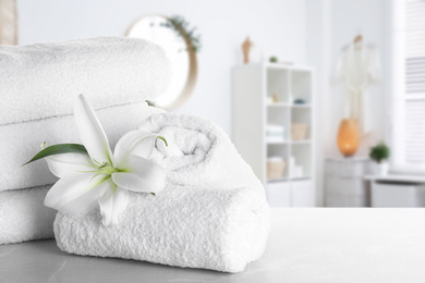 Fresh towels and lily flower on light grey marble table in bathroom. Space for text
