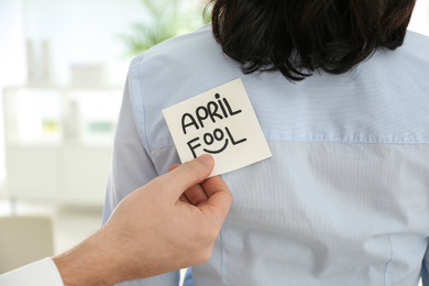 Man sticking APRIL FOOL note to colleague's back in office, closeup