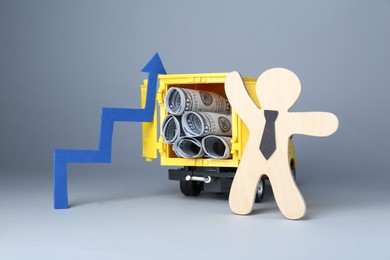 Economic profit. Wooden figure, arrow and toy truck with banknotes on light grey background