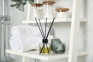 Photo of Aromatic reed air freshener, toiletries and rolled towels on white wooden shelf in bathroom