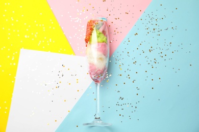 Glass with cotton candy on color background, top view