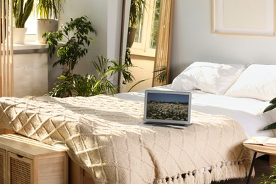 Photo of Stylish room interior with comfortable bed, houseplants and modern laptop