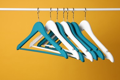 Empty clothes hangers on metal rail against yellow background
