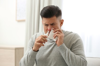 Ill man with paper tissue using nasal spray at home