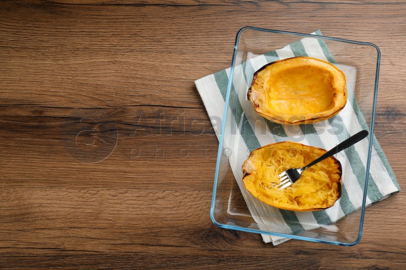 Halves of cooked spaghetti squash in baking dish on wooden table, top view Space for text