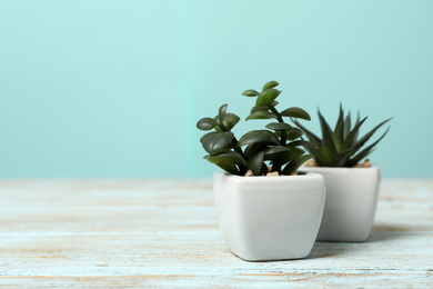 Artificial plants in white flower pots on light blue wooden table. Space for text