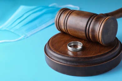 Wedding ring and judge hammer on light blue background, closeup. Divorce during coronavirus outbreak
