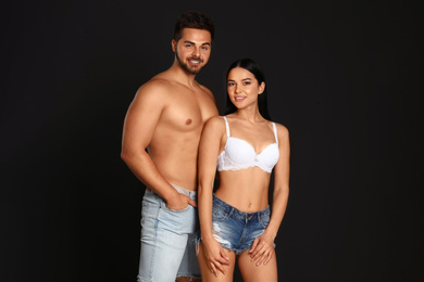 Young woman in underwear and denim shorts with her boyfriend on black background