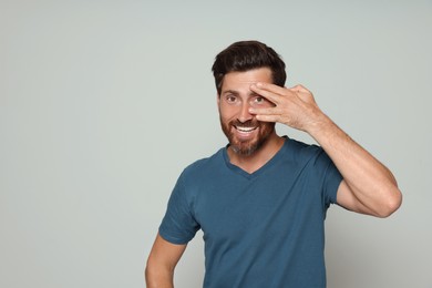 Photo of Smiling bearded man looking through spread fingers on grey background. Space for text