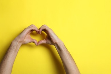Man making heart with his hands on yellow background, closeup. Space for text
