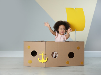 Photo of Cute African American child playing with cardboard ship near color wall