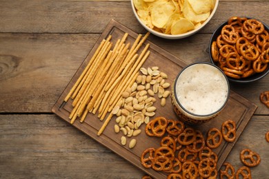 Glass of beer served with delicious pretzel crackers and other snacks on wooden table, flat lay