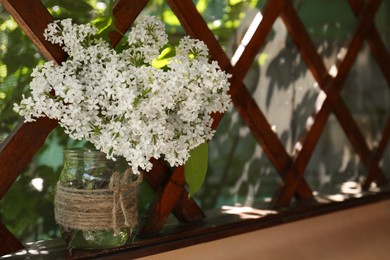 Photo of Beautiful lilac flowers in glass jar near window indoors. Space for text