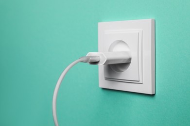 Power socket with inserted plug on turquoise wall, closeup. Electrical supply